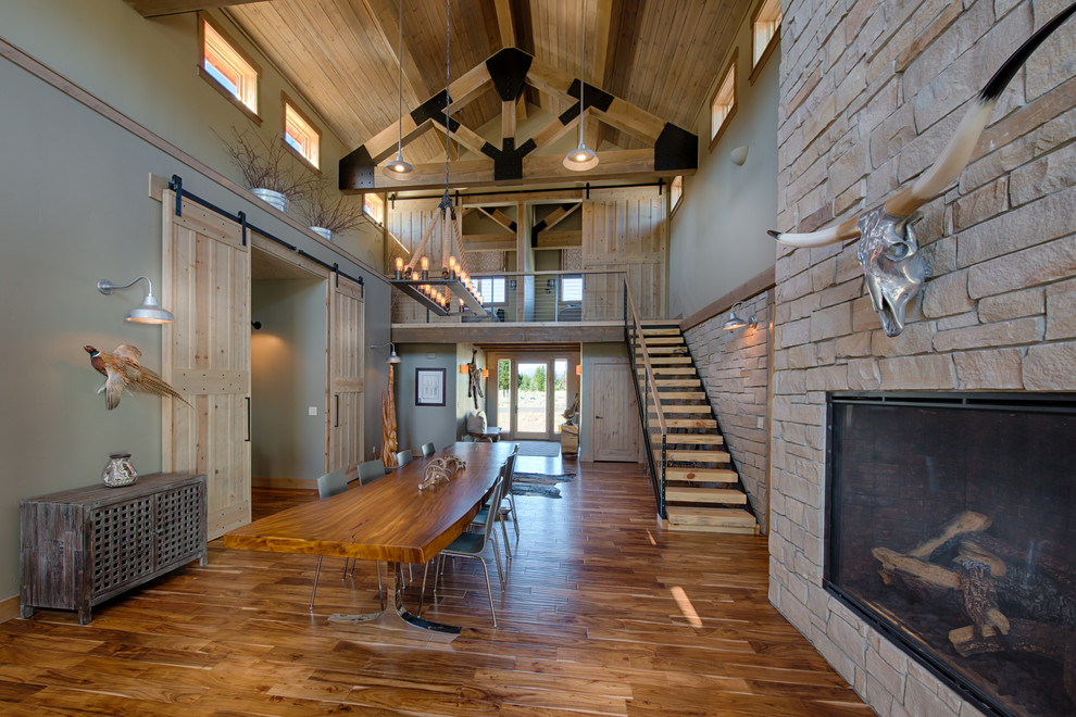 Inspiration pour une salle à manger ouverte sur le salon chalet avec un mur gris, un sol en bois brun, une cheminée standard et un manteau de cheminée en pierre.