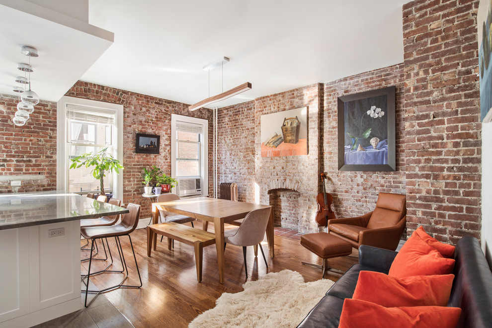 Cette photo montre une salle à manger ouverte sur le salon chic avec un mur rouge, un sol en bois brun, une cheminée standard et un manteau de cheminée en brique.