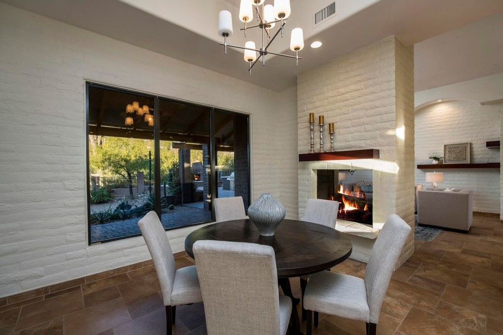 Example of a mid-sized trendy porcelain tile and brown floor enclosed dining room design in Phoenix with beige walls, a two-sided fireplace and a brick fireplace