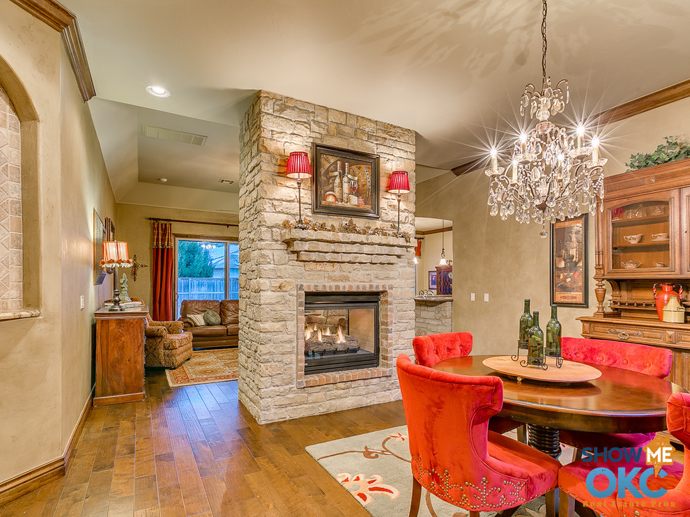 This is an example of a traditional dining room in Oklahoma City with medium hardwood flooring, a two-sided fireplace and a stone fireplace surround.