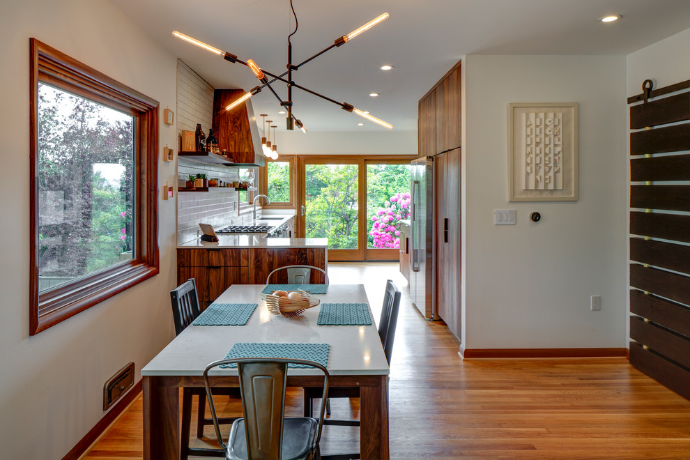 Cette image montre une salle à manger ouverte sur la cuisine traditionnelle avec un mur blanc et un sol en bois brun.