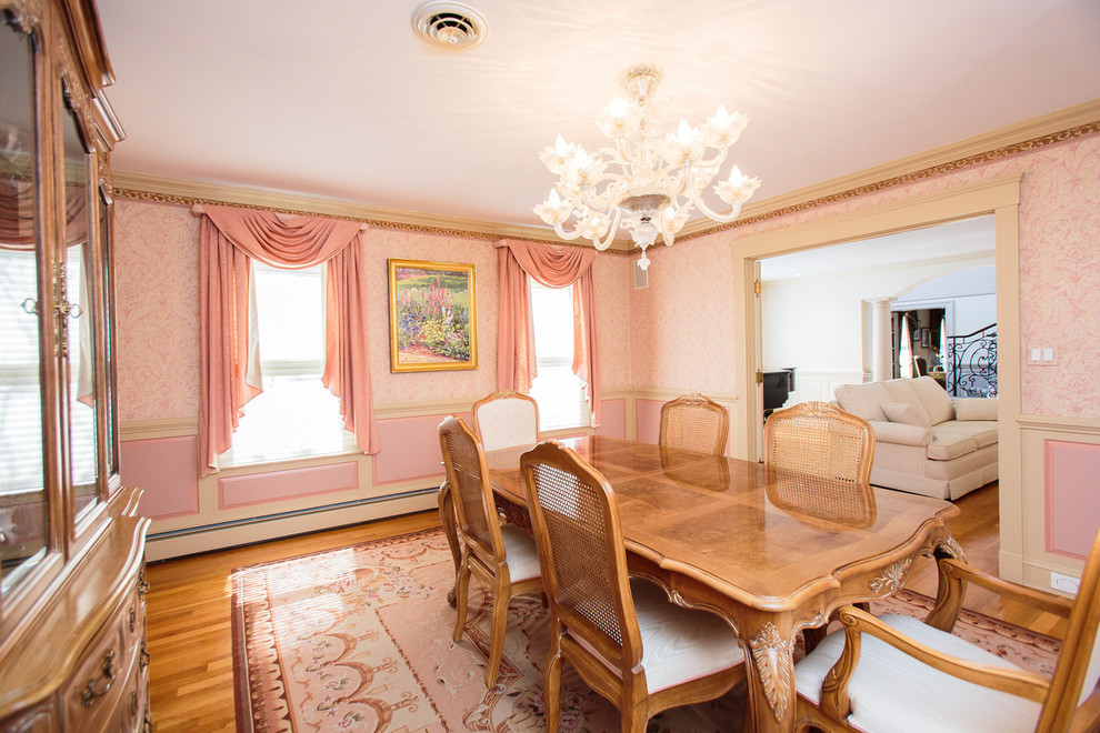 Cette photo montre une grande salle à manger chic fermée avec un mur rose et un sol en bois brun.