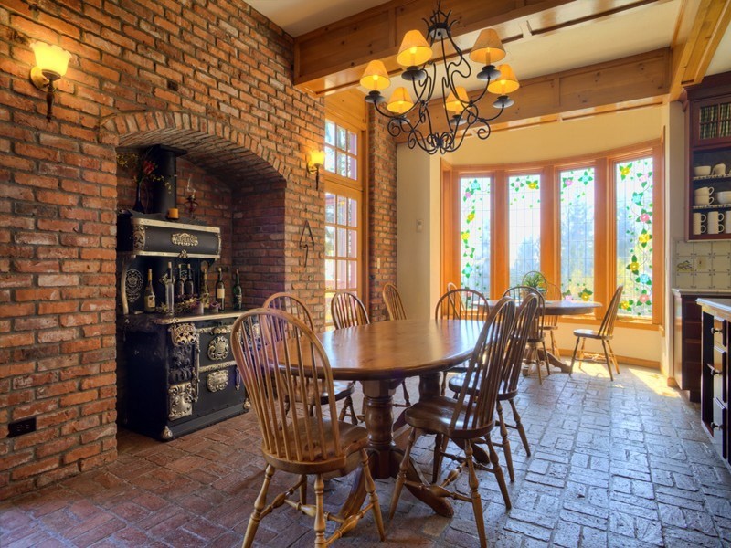 Immagine di una grande sala da pranzo aperta verso la cucina stile rurale con pareti beige, pavimento in mattoni, stufa a legna e cornice del camino in mattoni