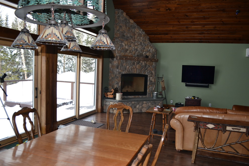 Inspiration pour une salle à manger ouverte sur le salon chalet de taille moyenne avec un mur vert, un sol en bois brun, une cheminée d'angle, un manteau de cheminée en pierre et un sol marron.