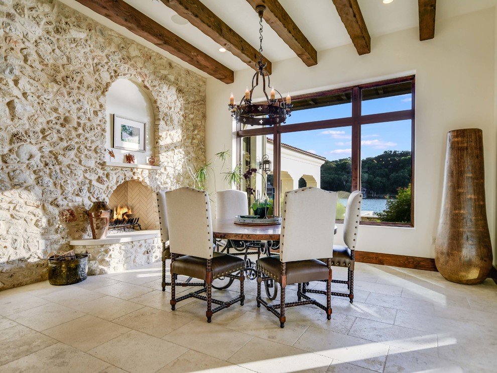 Ispirazione per una sala da pranzo mediterranea con pareti bianche, camino classico, cornice del camino in pietra e pavimento beige