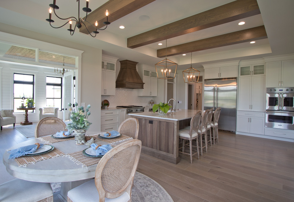 Foto di una sala da pranzo aperta verso la cucina con pareti bianche, parquet chiaro, pavimento marrone e travi a vista