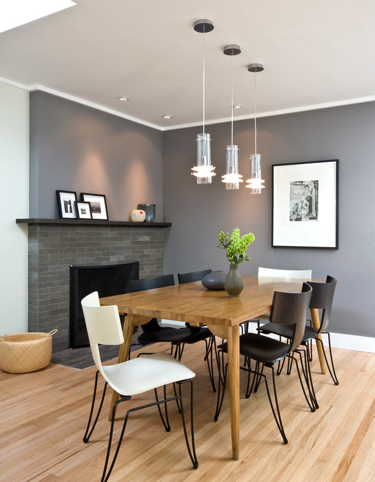 На фото: столовая в современном стиле с серыми стенами, светлым паркетным полом и фасадом камина из плитки с
