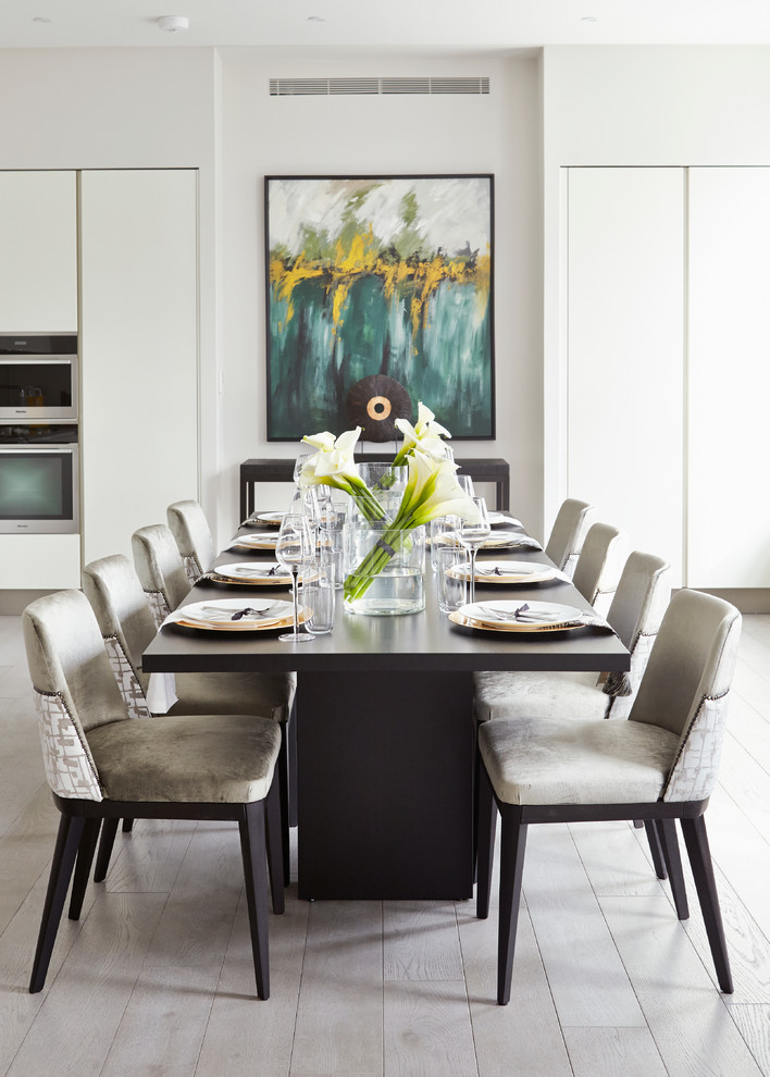 Réalisation d'une salle à manger ouverte sur la cuisine design avec un mur blanc et parquet clair.