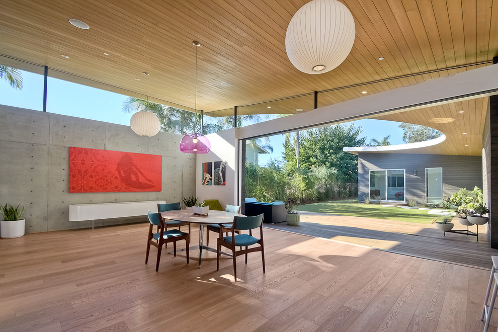 Example of a mid-century modern light wood floor dining room design in San Diego with white walls and a plaster fireplace