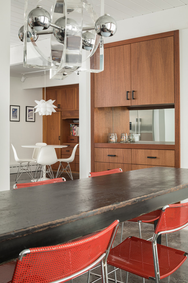 This is an example of a retro open plan dining room in Portland Maine with white walls, concrete flooring and a timber clad ceiling.