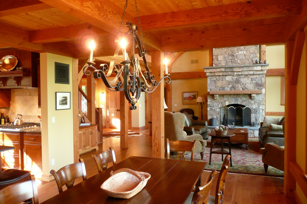 Réalisation d'une grande salle à manger ouverte sur le salon chalet avec un mur jaune, un sol en bois brun, une cheminée standard et un manteau de cheminée en pierre.