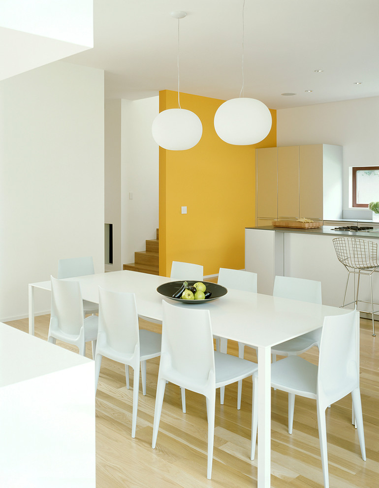 Cette photo montre une salle à manger ouverte sur la cuisine moderne avec un mur jaune, parquet clair et aucune cheminée.