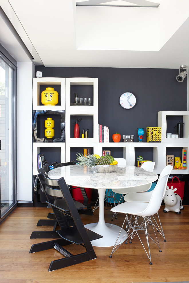 Design ideas for an eclectic dining room in London with black walls and medium hardwood flooring.