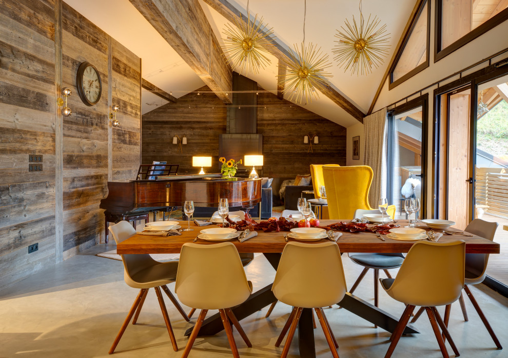 Cette image montre une très grande salle à manger ouverte sur le salon chalet avec un mur multicolore, sol en béton ciré, un poêle à bois, un manteau de cheminée en pierre et un sol gris.