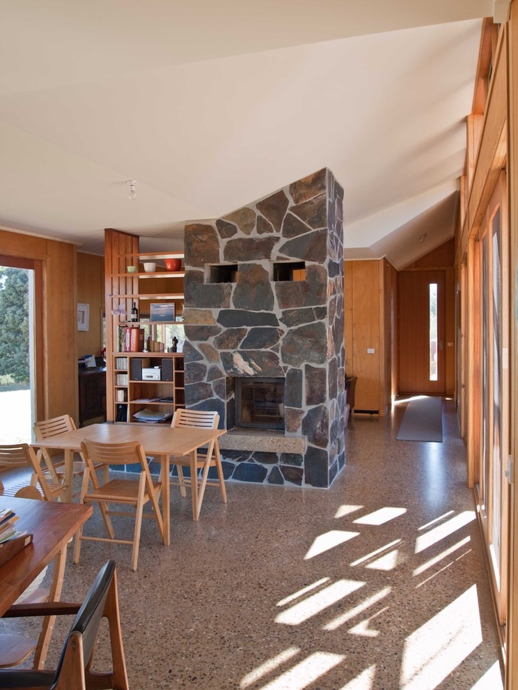 Diseño de comedor moderno grande abierto con paredes beige, suelo de cemento, chimenea de doble cara, marco de chimenea de piedra y suelo beige