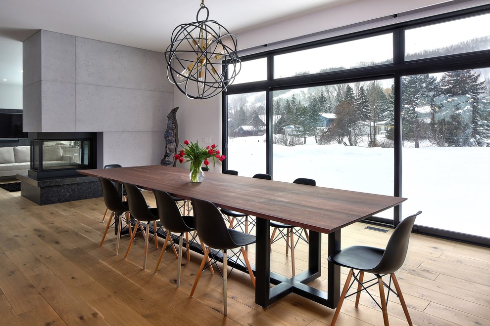 Cette image montre une salle à manger ouverte sur le salon design avec un mur blanc, parquet clair, une cheminée double-face et un manteau de cheminée en béton.