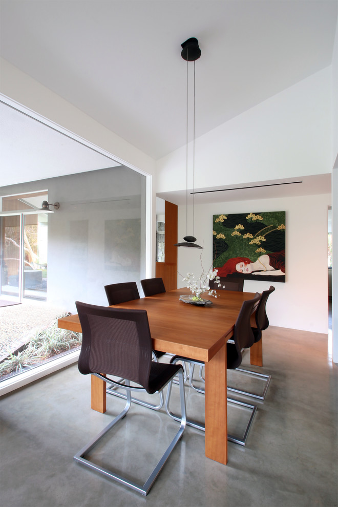 Cette image montre une salle à manger ouverte sur le salon vintage avec un mur blanc et sol en béton ciré.