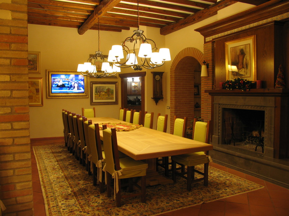 Modelo de comedor tradicional grande abierto con paredes beige, suelo de baldosas de terracota, todas las chimeneas y marco de chimenea de piedra