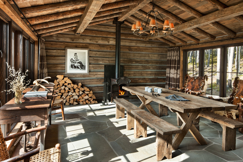 Esempio di una sala da pranzo rustica con pareti marroni, stufa a legna e pavimento grigio