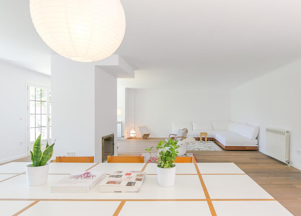 Стильный дизайн: большая гостиная-столовая в скандинавском стиле с белыми стенами, паркетным полом среднего тона и стандартным камином - последний тренд