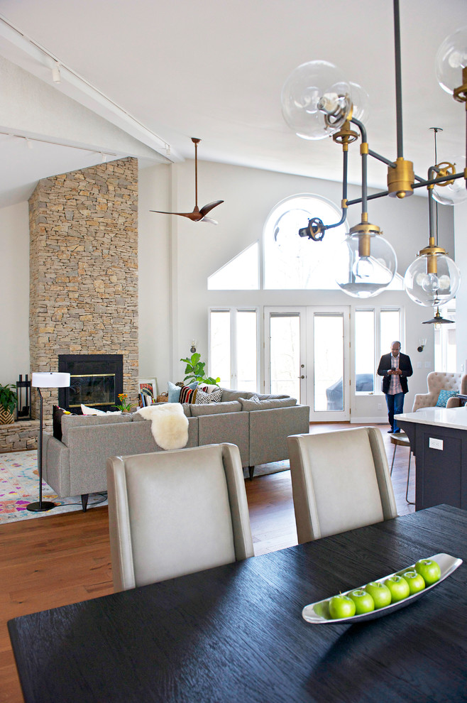 Источник вдохновения для домашнего уюта: большая гостиная-столовая в стиле неоклассика (современная классика) с серыми стенами, паркетным полом среднего тона, печью-буржуйкой и фасадом камина из камня