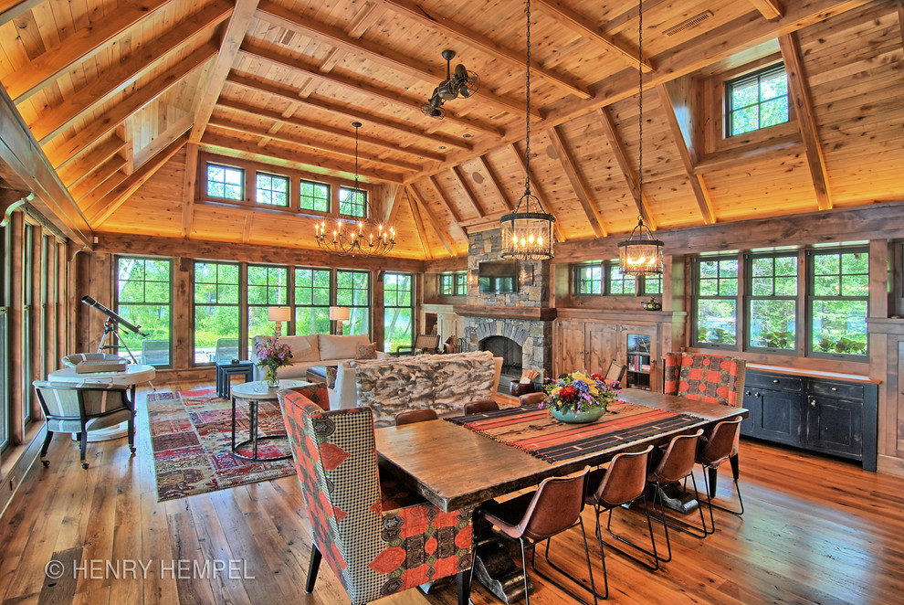 Cette photo montre une grande salle à manger ouverte sur le salon montagne avec un mur marron, un sol en bois brun, une cheminée standard et un manteau de cheminée en pierre.