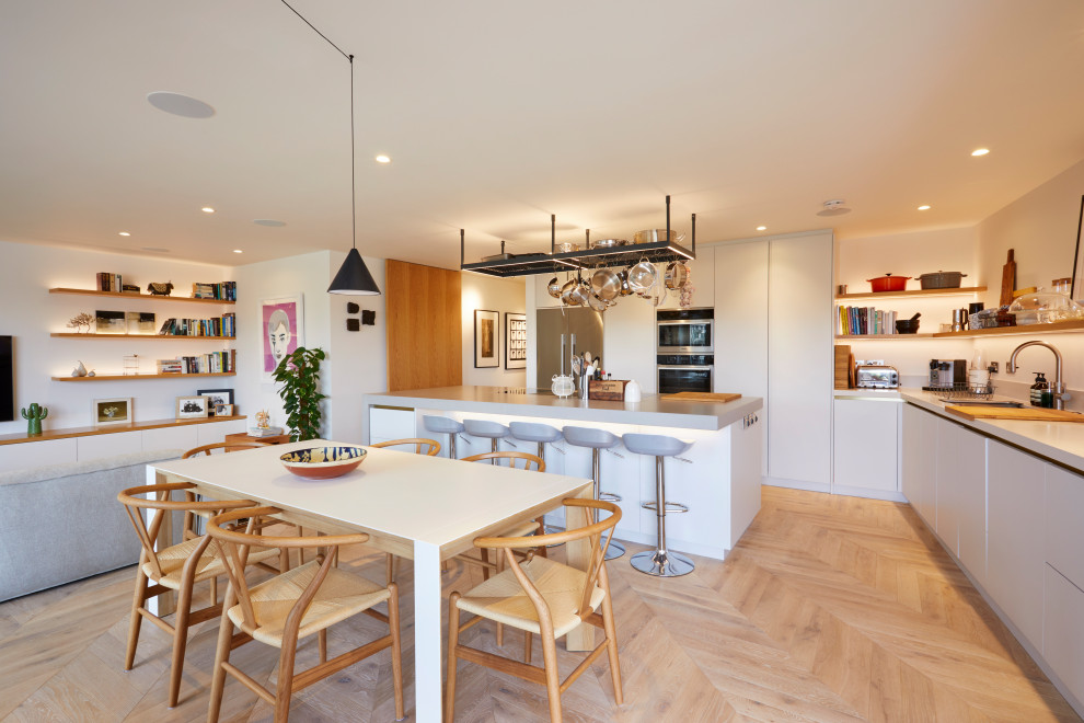 Cette image montre une salle à manger ouverte sur la cuisine avec un mur blanc, un sol en bois brun et un sol beige.
