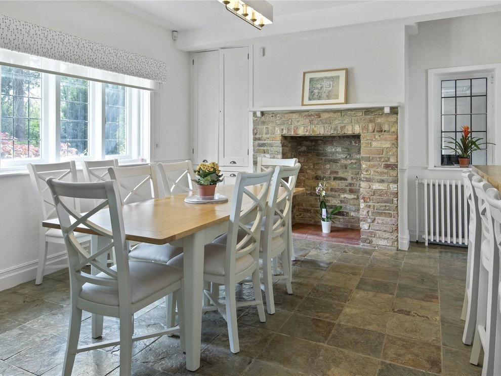 Design ideas for a medium sized rural dining room in Surrey with white walls, a standard fireplace, a brick fireplace surround and grey floors.