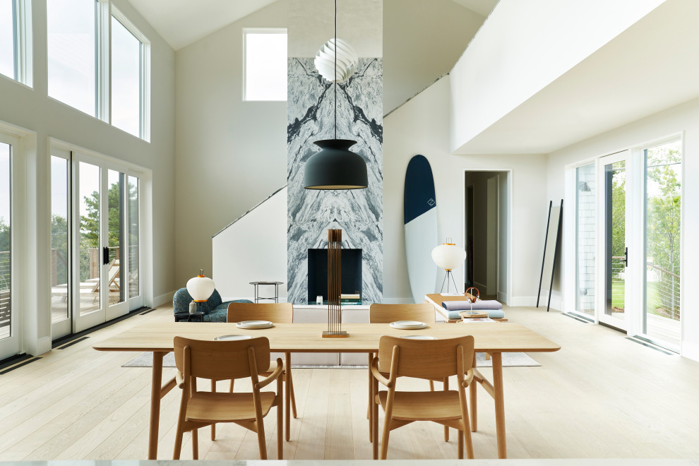 Exemple d'une salle à manger ouverte sur le salon tendance avec un mur blanc, parquet clair, une cheminée standard, un manteau de cheminée en pierre, un sol blanc et un plafond voûté.