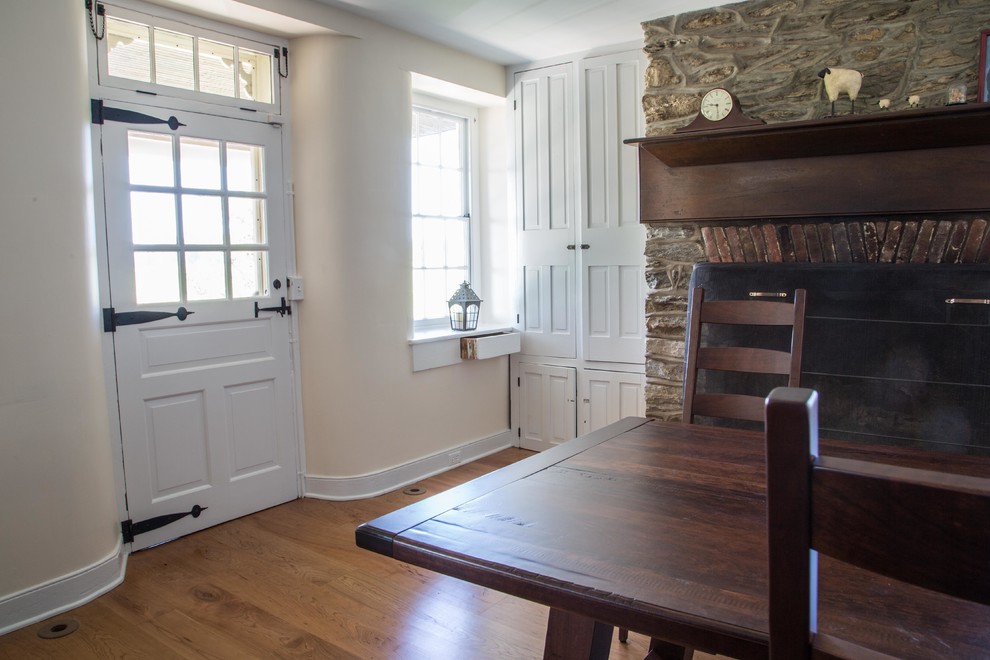 Ejemplo de comedor de cocina campestre con paredes blancas, suelo de madera en tonos medios, marco de chimenea de piedra y todas las chimeneas
