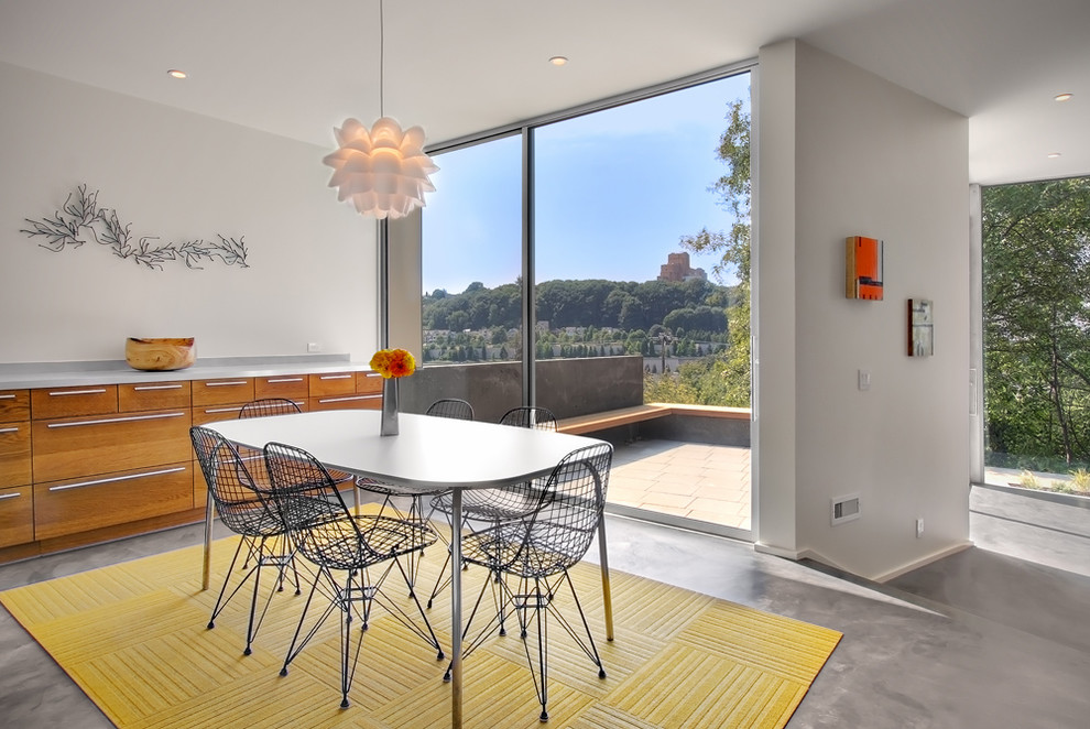 Cette image montre une salle à manger ouverte sur la cuisine design de taille moyenne avec sol en béton ciré, un mur blanc, aucune cheminée et un sol gris.