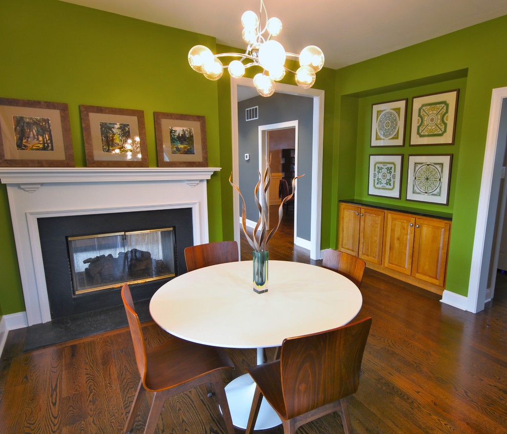 Immagine di una piccola sala da pranzo aperta verso la cucina moderna con parquet scuro, camino bifacciale, cornice del camino in pietra e pareti verdi