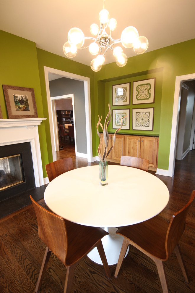 Exemple d'une petite salle à manger ouverte sur la cuisine rétro avec parquet foncé, une cheminée double-face, un manteau de cheminée en pierre et un mur vert.