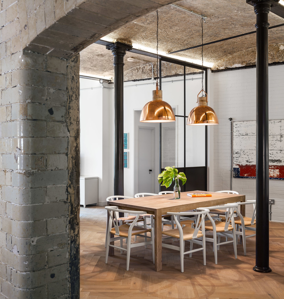 Foto di una sala da pranzo aperta verso il soggiorno industriale con parquet chiaro e pareti bianche