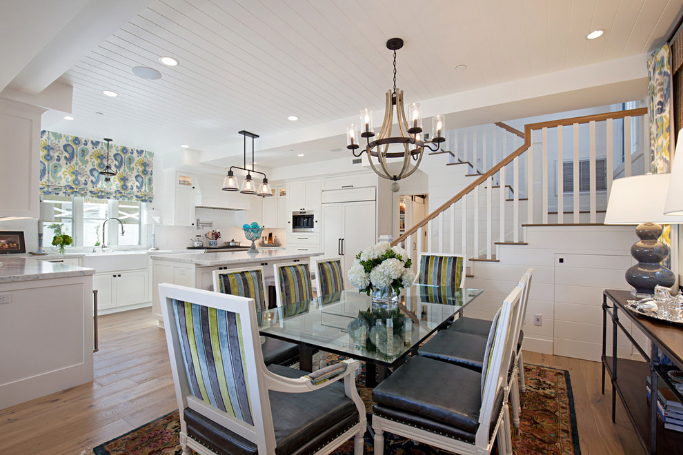 Aménagement d'une salle à manger ouverte sur la cuisine bord de mer avec un mur blanc et un sol en bois brun.