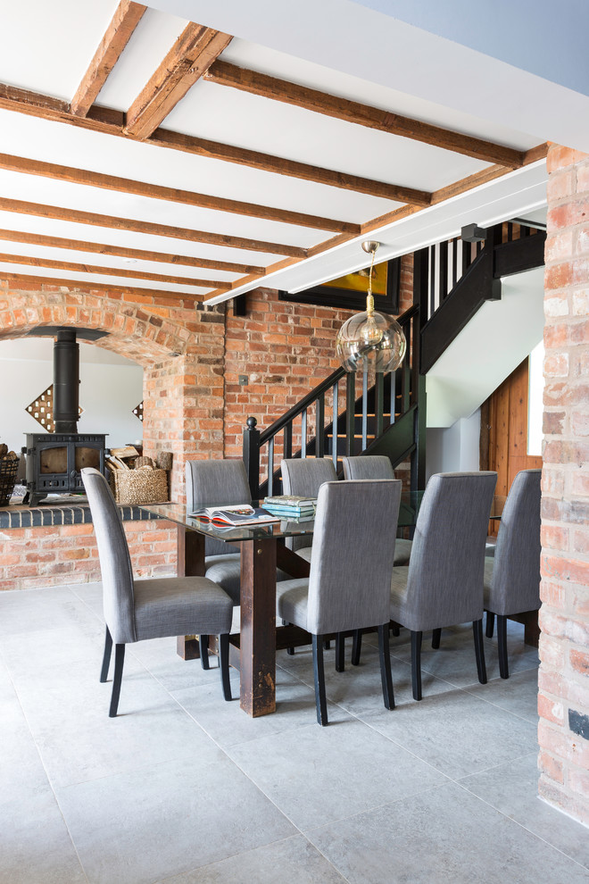 This is an example of a medium sized farmhouse open plan dining room with a wood burning stove, grey floors and white walls.