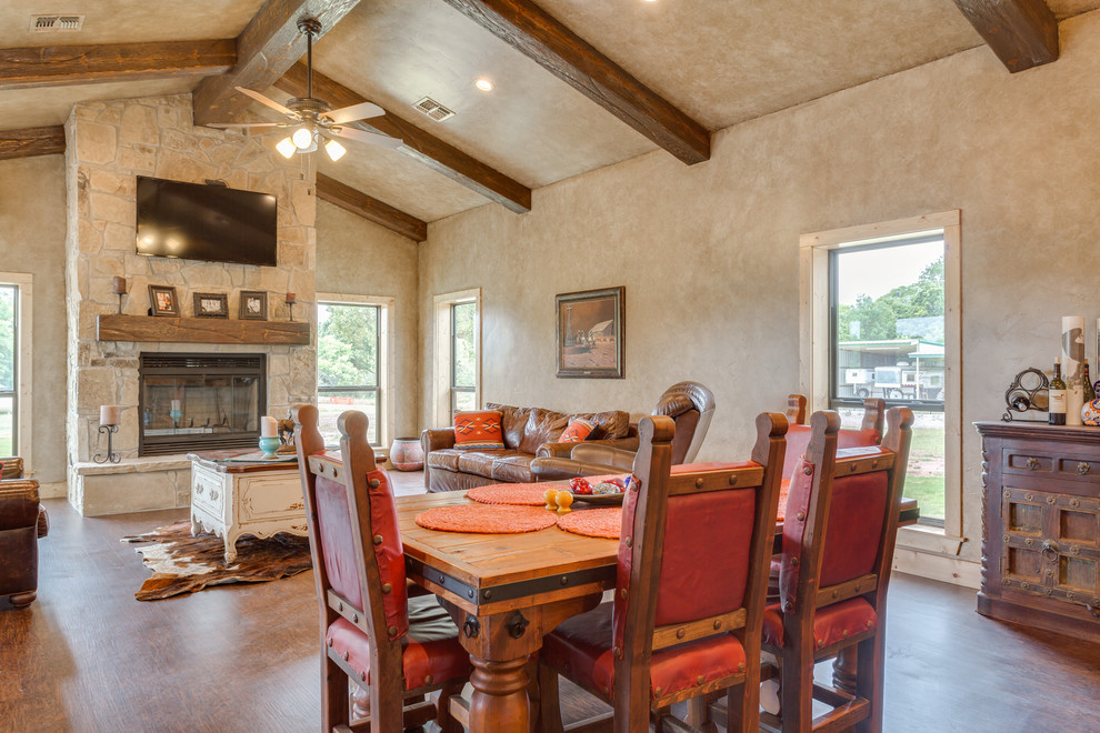 Aménagement d'une salle à manger ouverte sur le salon montagne de taille moyenne avec un mur beige, un sol en vinyl, une cheminée standard, un manteau de cheminée en pierre et un sol marron.