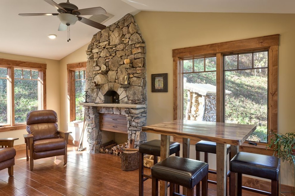 Cette photo montre une salle à manger ouverte sur la cuisine craftsman de taille moyenne avec un mur beige, parquet foncé, une cheminée standard, un manteau de cheminée en pierre et un sol marron.
