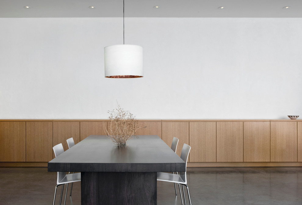 Cette photo montre une petite salle à manger ouverte sur le salon moderne avec un mur blanc, sol en béton ciré, une cheminée standard et un manteau de cheminée en métal.