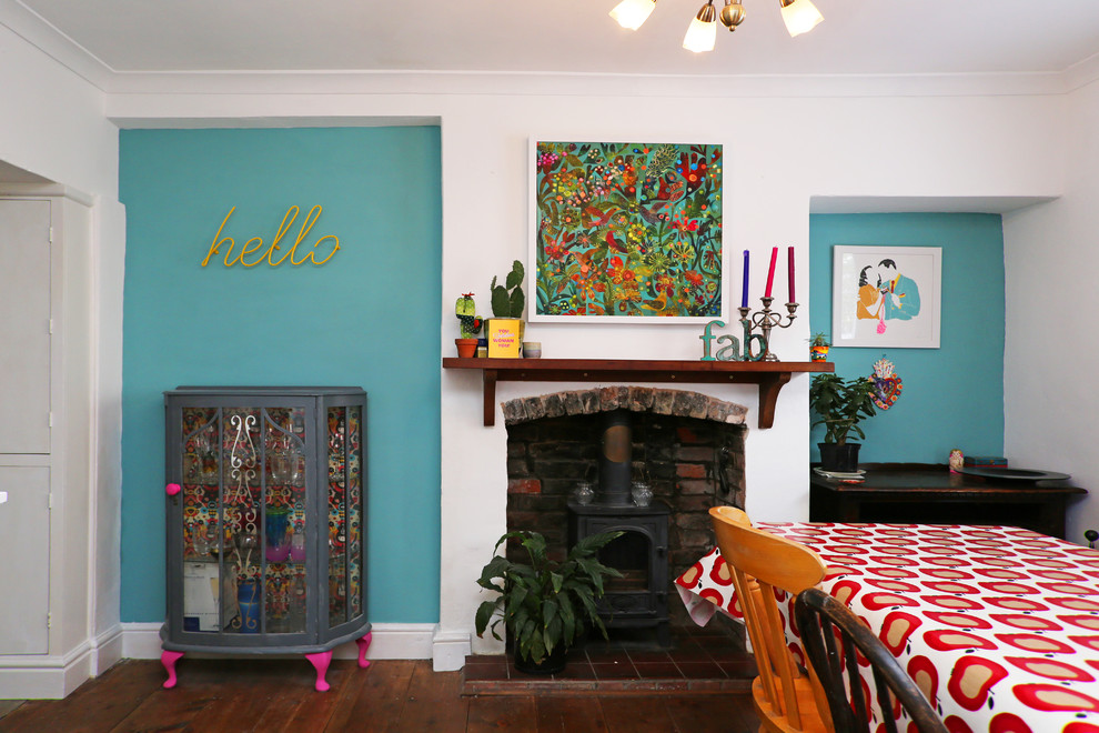 Exemple d'une salle à manger ouverte sur la cuisine éclectique de taille moyenne avec un mur multicolore, parquet foncé, un poêle à bois, un manteau de cheminée en bois et un sol marron.