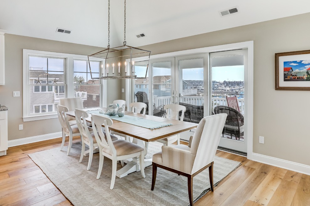 Exemple d'une salle à manger ouverte sur la cuisine bord de mer avec un mur gris, parquet clair et un sol beige.