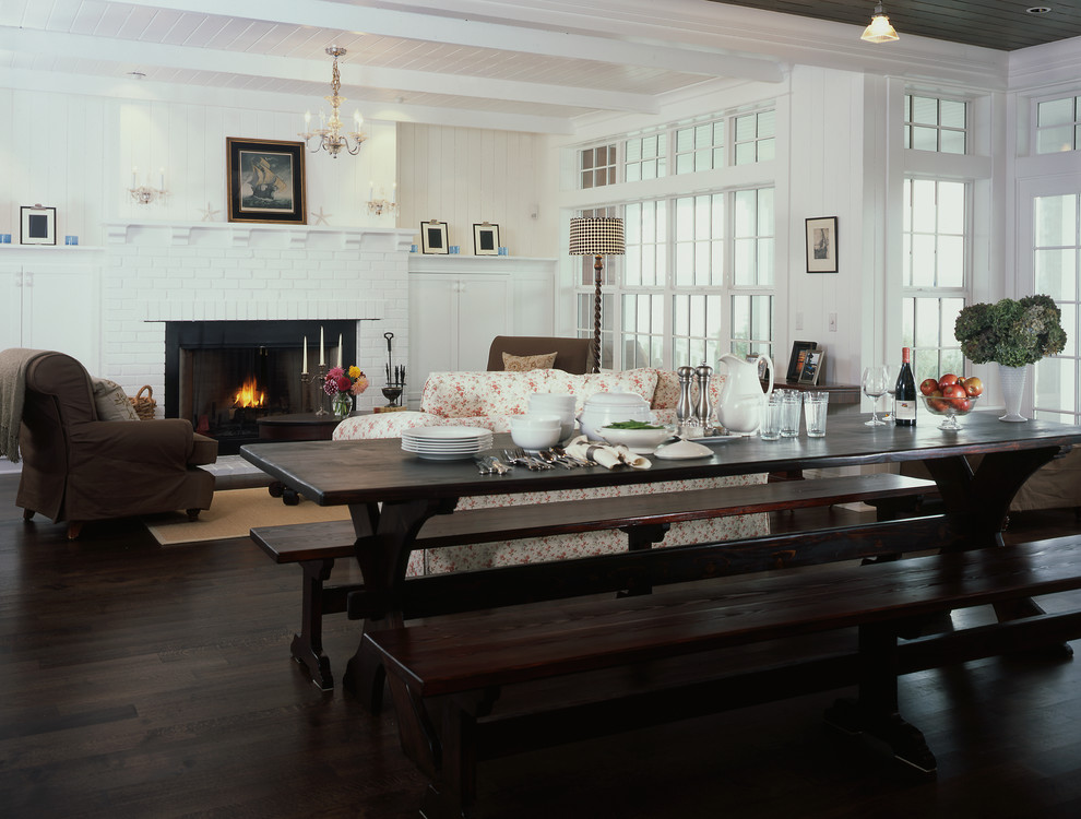 Immagine di una grande sala da pranzo aperta verso il soggiorno costiera con pareti bianche, parquet scuro, camino classico e cornice del camino in mattoni