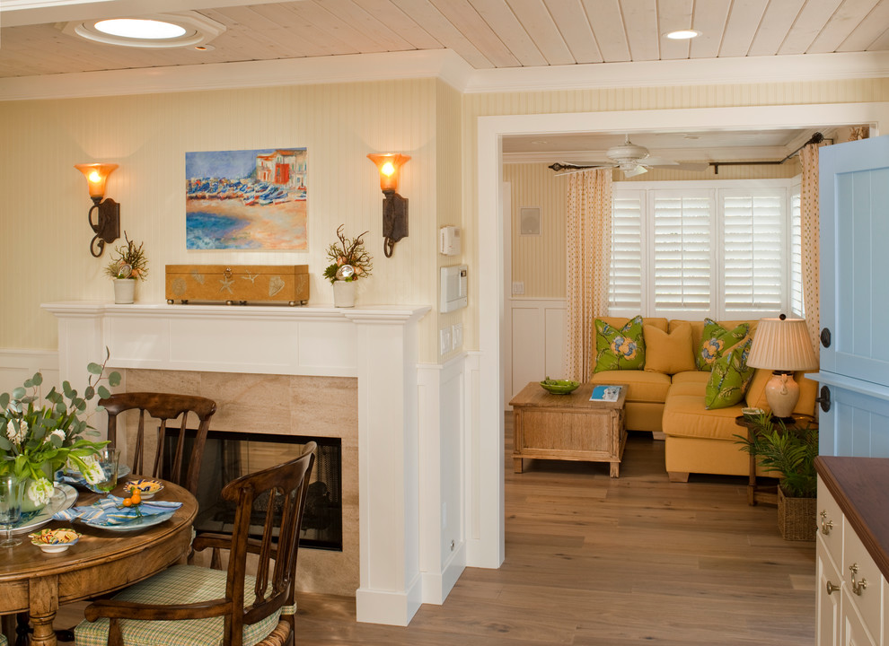 Inspiration pour une salle à manger ouverte sur la cuisine marine avec un mur jaune, parquet clair, une cheminée double-face et un manteau de cheminée en pierre.
