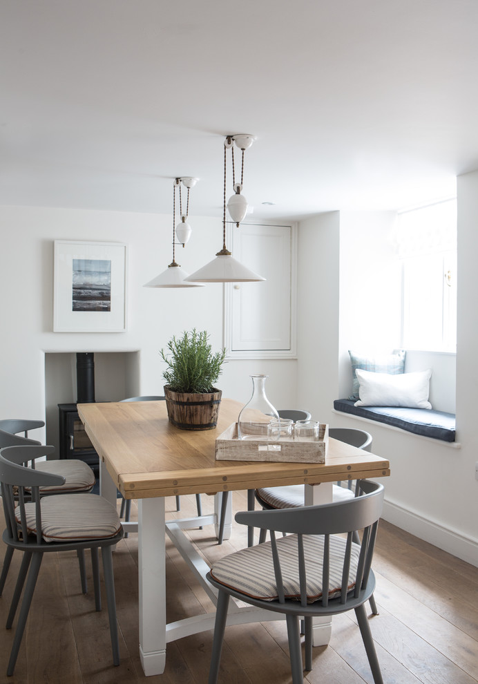 Inspiration for a coastal dining room in London with white walls, light hardwood flooring and a wood burning stove.