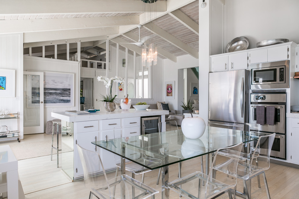 Cette photo montre une grande salle à manger ouverte sur la cuisine bord de mer avec un mur blanc et parquet clair.