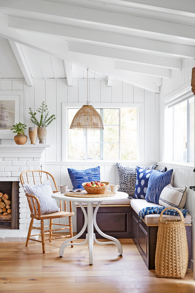 Example of a small beach style light wood floor dining room design in Los Angeles with white walls, a standard fireplace and a brick fireplace