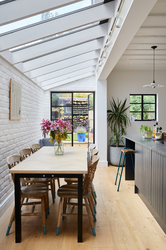 Cette image montre une salle à manger ouverte sur la cuisine design avec un mur blanc, parquet clair, un sol beige et un mur en parement de brique.