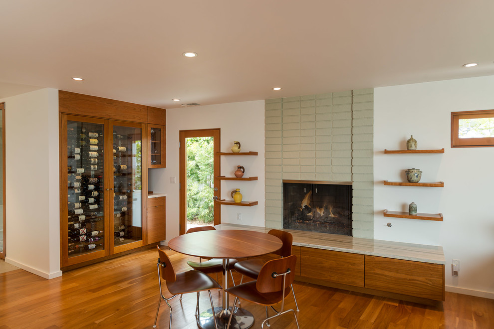 Inspiration pour une salle à manger ouverte sur la cuisine minimaliste de taille moyenne avec un manteau de cheminée en béton, un mur blanc, parquet foncé, une cheminée standard et un sol marron.