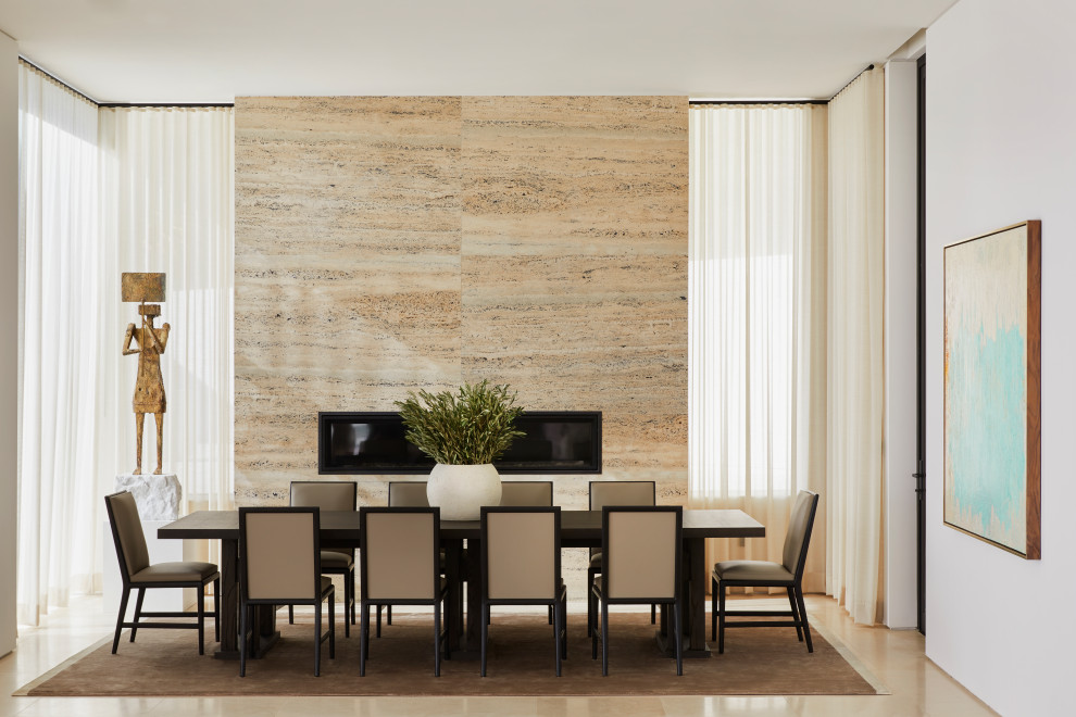 Cette image montre une salle à manger design avec un mur blanc, une cheminée ribbon, un manteau de cheminée en pierre et un sol beige.