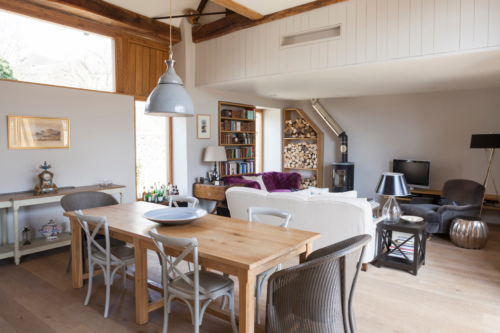 Immagine di una sala da pranzo aperta verso il soggiorno minimalista di medie dimensioni con pareti grigie, parquet chiaro e stufa a legna